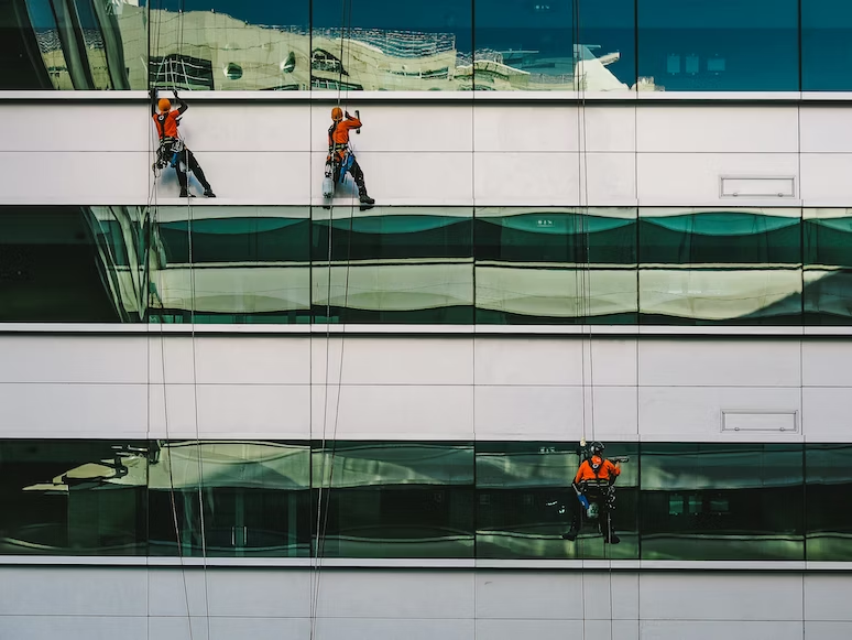pegawai pemeliharaan gedung sedang membersihkan kaca gedung sebuah perusahaan
